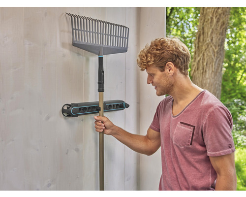 Un râteau est suspendu à un support à outils sur le mur.