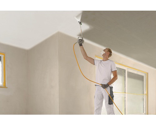 Un homme utilise un pistolet à peinture pour peindre un plafond lors de la rénovation d''une pièce.