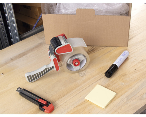 Carton, dérouleur de ruban adhésif, marqueur, bloc-notes et cutter sur une table.