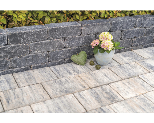 Gestapelte Mauersteine bilden eine kleine Mauer, ergänzt durch Gehwegplatten und dekorative Elemente