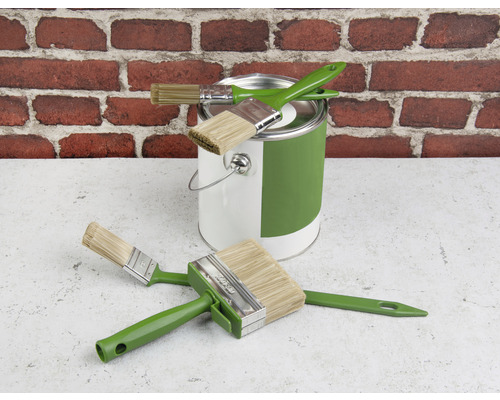 Farbeimer und verschiedene Pinsel vor einer Ziegelwand