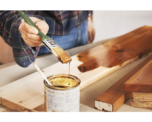 Auftragen von Holzschutzlasur mit Pinsel auf ein Holzbrett