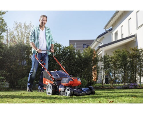 Un homme tond la pelouse avec une tondeuse Einhell dans le jardin.