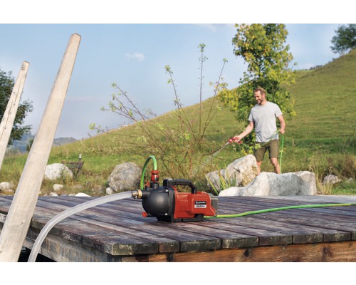 Station de pompage domestique Einhell sur un ponton en bois avec un homme arrosant avec un tuyau d'arrosage à l'arrière-plan