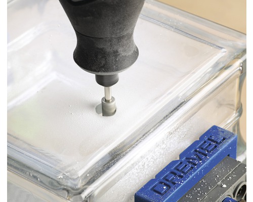 Un outil perce un trou dans un pavé de verre fixé dans un étau