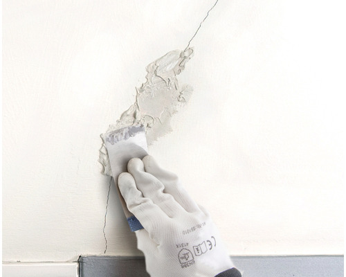 Une fissure dans un mur est colmatée avec une spatule.