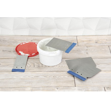 Mastic dans un seau avec des spatules sur un plancher en bois