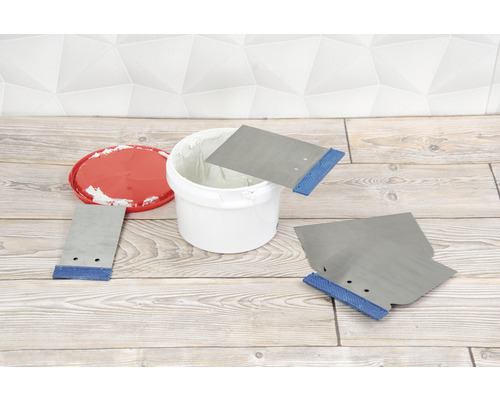 Mastic dans un seau avec des spatules sur un plancher en bois