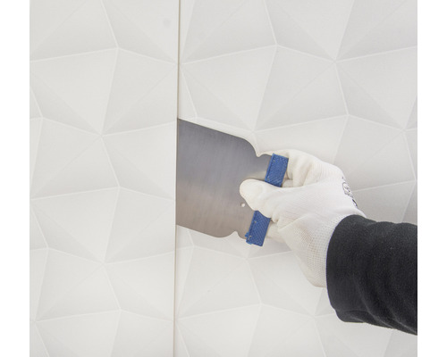 Une main gantée lisse un papier peint avec une spatule.