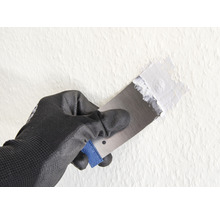 Main avec gant de travail et spatule appliquant du mastic sur le mur