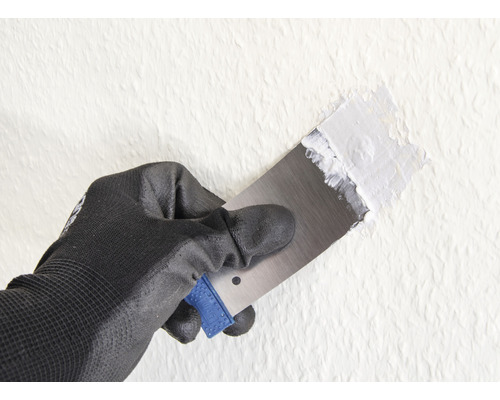 Main avec gant de travail et spatule appliquant du mastic sur le mur