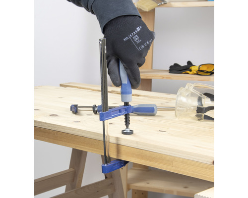 Un serre-joint fixe deux pièces de bois sur un établi.