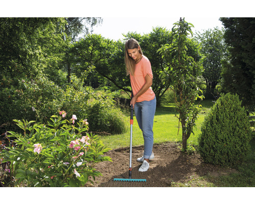 Une femme utilise un râteau dans le jardin pour travailler le sol.