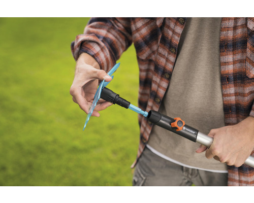 Eine Person befestigt einen Gardena-Gartenbewässerungsaufsatz an einem Bewässerungsrohr.