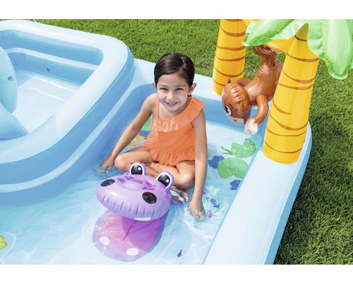 Fille jouant dans une pataugeoire gonflable avec toboggan, palmier et singe