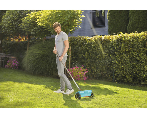 Ein Mann verwendet einen Streuwagen im Garten für die Rasenpflege.