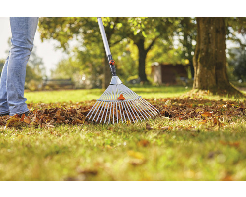 Eine Person harkt Laub mit einem Laubbesen im Garten.