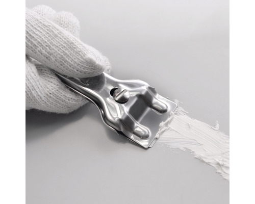 Une main gantée de blanc tient un couteau à mastic en métal qui étale du mastic sur une surface.