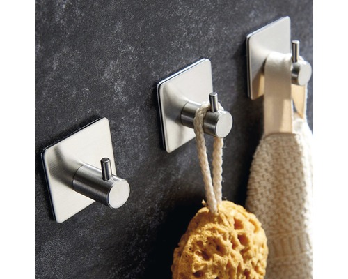 Trois crochets autocollants en acier inoxydable fixés à un mur, avec une éponge et une serviette dessus.