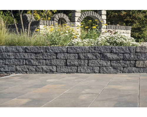 Mur de jardin en pierres de parement avec des plantes et des arches en pierre en arrière-plan