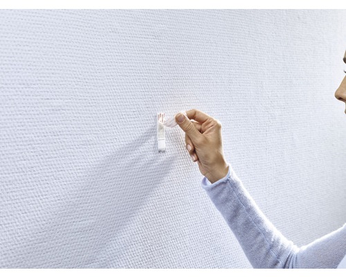 Une femme fixe un crochet adhésif sur un mur