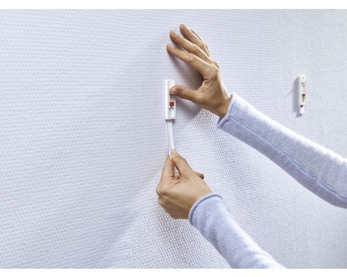 Une personne fixe un crochet adhésif sur un mur.