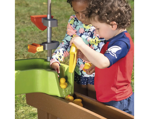 Deux enfants jouent dehors avec un circuit d''eau et des canards en plastique.