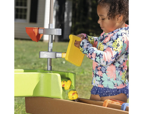 Fille jouant avec une table de jeu d''eau avec des canards jaunes et un seau dans le jardin