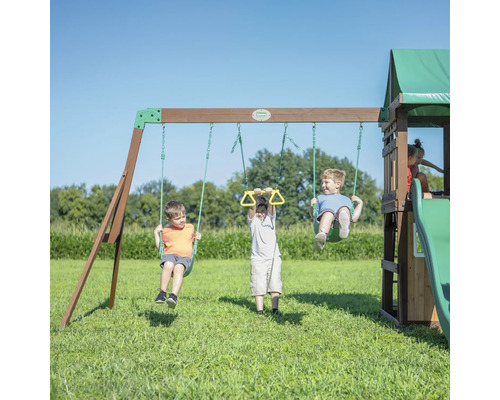 Des enfants jouent sur une aire de jeux avec des balançoires, des anneaux de gymnastique, un toboggan et une cabane de jeu.