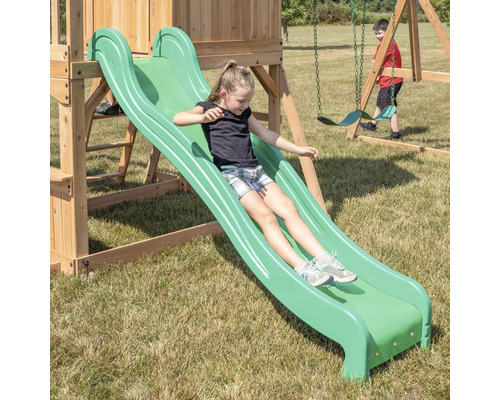 Une fille glisse sur un toboggan vert d''une tour de jeux en bois