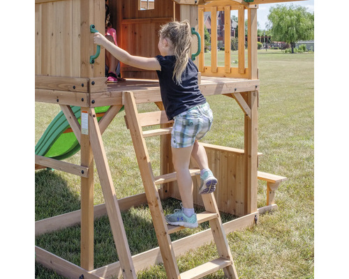 Une fille grimpe sur une tour de jeu en bois avec toboggan et table de pique-nique