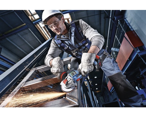 Un homme portant des lunettes de sécurité, un casque et des gants meule du métal avec une meuleuse d'angle, des étincelles volent