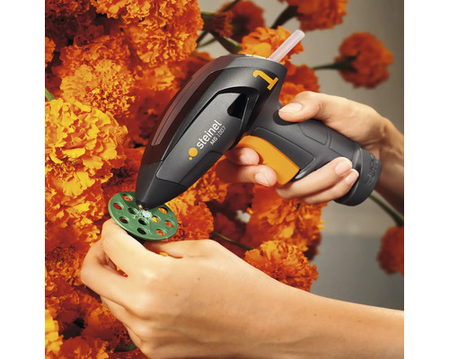 Heissklebepistole bei der Anwendung auf einem Bastelprojekt mit Blumen