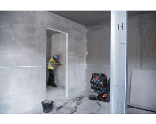 Ein Arbeiter benutzt einen Linienlaser in einem Rohbau, um eine gerade Linie an einer Wand zu markieren.