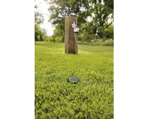 Scène avec un capteur d''irrigation dans l''herbe et un robinet d''eau en arrière-plan.