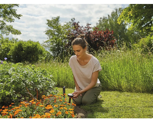 Une femme agenouillée dans le jardin utilise un capteur d''humidité entre des parterres de fleurs