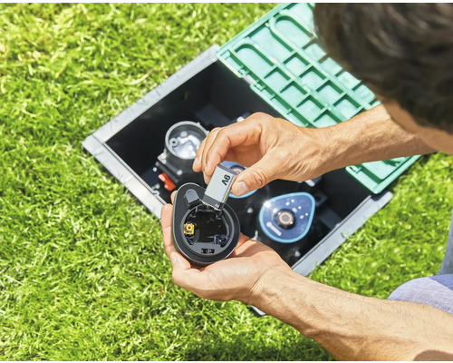 Une personne insère une pile dans un ordinateur d''arrosage dans le jardin