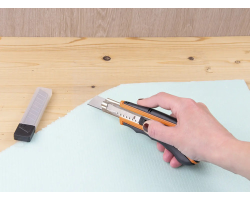 Une main coupe une plaque isolante avec un cutter.