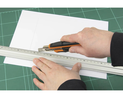 Une personne coupe du papier avec un cutter et une règle sur un tapis de découpe