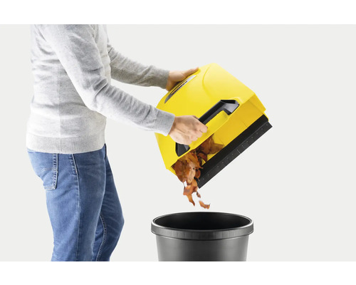 Une personne vide un collecteur de feuilles jaune dans une poubelle noire.