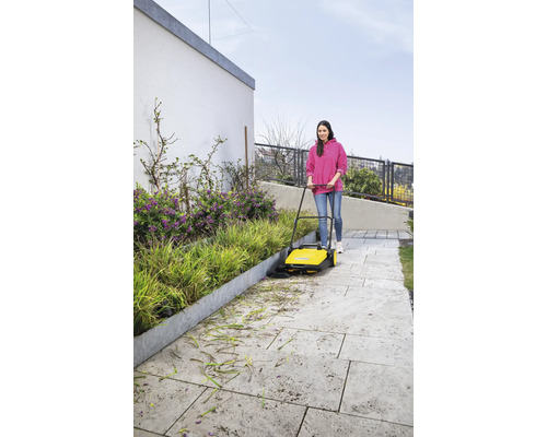 Une femme balaie une allée de feuilles et de fleurs avec une balayeuse