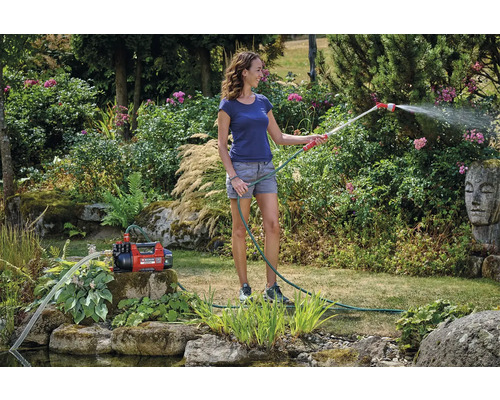 Femme arrose le jardin avec une pompe de jardin et un tuyau d''arrosage