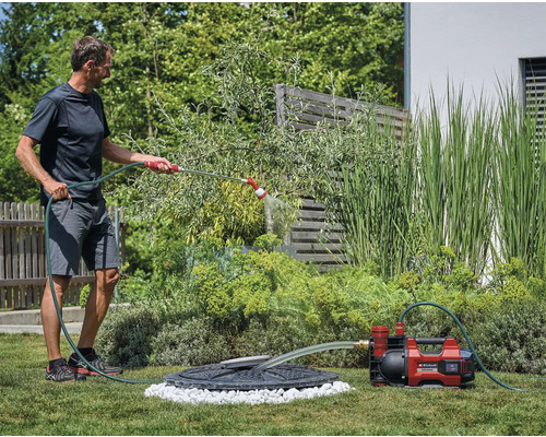 Homme arrose le jardin avec une pompe de jardin et un tuyau d''arrosage