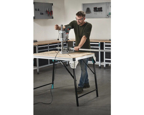 Un homme travaille avec une perceuse sur un établi dans un atelier.