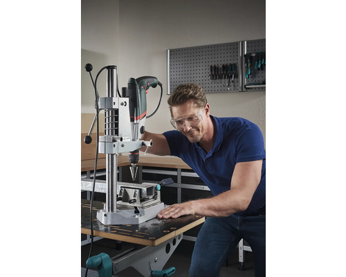 Un homme portant des lunettes de sécurité utilise une perceuse à colonne dans un atelier.