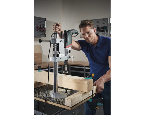 Un homme perce un trou dans une pièce de bois avec une perceuse et un support de perceuse.