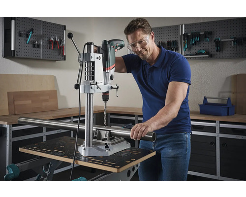 Un homme perce un tube avec une perceuse à colonne dans un atelier.