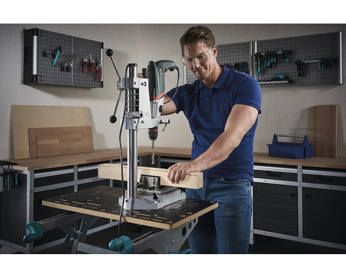 Un homme travaille avec une perceuse à colonne sur une pièce de bois dans un atelier