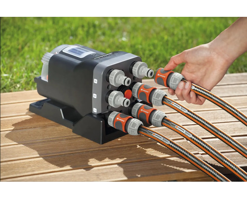Distributeur d''eau automatique Gardena avec six raccords et tuyaux d''arrosage connectés sur une surface en bois
