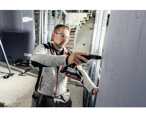 Artisan fixant une plaque de plâtre avec une visseuse sans fil pour cloisons sèches